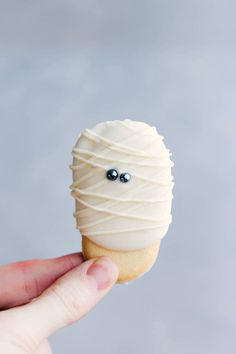 a hand holding up a white frosted pastry with eyes on it's side