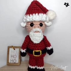 a crocheted santa clause doll sitting on top of a wooden table next to a sign