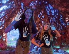 two women with painted hands are standing in front of a fake tree and another woman is holding out her hand