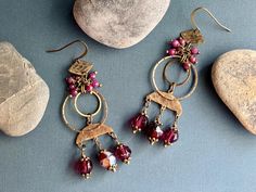 Check out these boho chandelier earrings, crafted with tiny faceted ruby red chalcedony beads, vibrant red glass beads, and raw brass. These earrings highlight a variety of dangling brass shapes which I've hammered, stamped, and given a patina finish to add a rustic charm that perfectly complements the rich red stones and beads. Red chalcedony is believed to bring vitality and passion to life. It's thought to encourage confidence and emotional balance, promoting strength and resilience. I chose this stone for its deep, captivating color and its powerful energy, which I hope will inspire you every time you wear these earrings! -Made just for you in my Brooklyn studio -Antique brass French ear wires are nickel free, lead free, and EU compliant base metal brass -Earrings measure around 3 3/8" Red Bohemian Chandelier Earrings Nickel-free, Red Bohemian Nickel-free Chandelier Earrings, Bohemian Red Nickel-free Chandelier Earrings, Red Bohemian Chandelier Earrings For Pierced Ears, Red Bohemian Chandelier Earrings, Bohemian Red Chandelier Earrings, Handmade Ruby Dangle Earrings, Bohemian Chandelier Earrings With Dangling Beads, Handmade Bohemian Ruby Jewelry