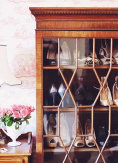 a wooden shelf filled with lots of shoes next to a vase full of pink flowers