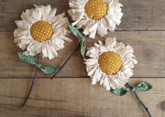 three white and yellow flowers with green stems on wooden floor next to wood planks