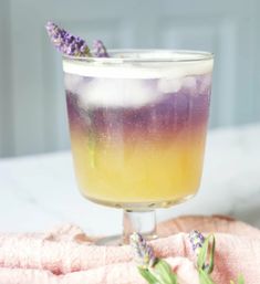 a glass filled with liquid sitting on top of a pink towel next to lavender flowers