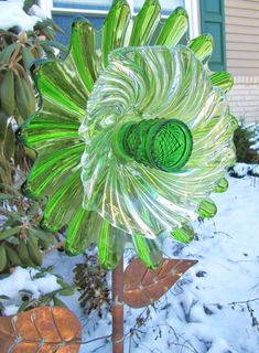 a green glass flower sitting on top of a snow covered ground next to a house