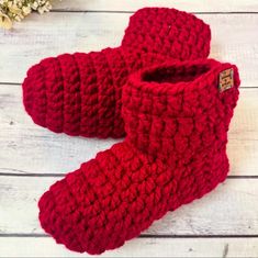 red crocheted booties sitting on top of a white wooden floor next to flowers