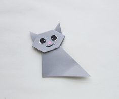 an origami cat with big eyes on it's head is shown in grey paper