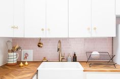 a kitchen with white cabinets and pink tile backsplash, gold faucets