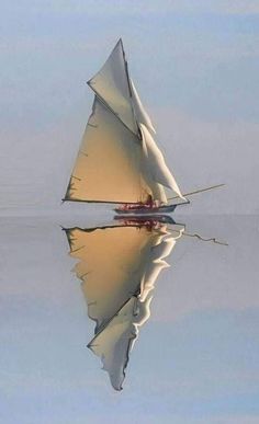 a sailboat floating on top of a body of water with its reflection in the water