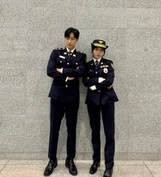 two uniformed men standing next to each other in front of a wall with his arms crossed