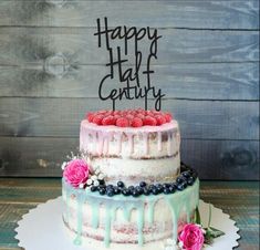 a wedding cake with two hearts on top and blueberries in the bottom, sitting on a wooden table