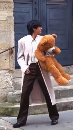 a woman holding a large brown teddy bear on the side of a building with blue doors