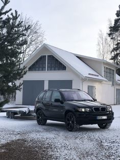 a black car is parked in front of a white house with snow on the ground