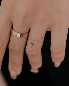 a woman's hand with a small cross tattoo on the middle finger and a tiny diamond ring