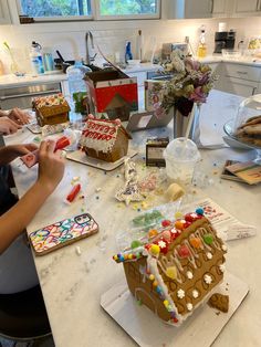 two people decorating gingerbread houses on a kitchen counter