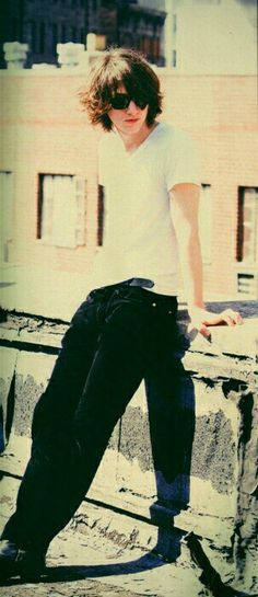 a young man in white shirt and black pants standing on top of a building with his legs crossed