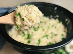 a wooden spoon full of food in a black crock pot with parsley on top