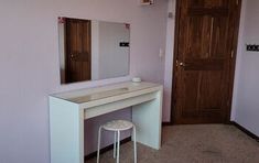 a white dressing table with stool and mirror in a pink walled room next to a wooden door