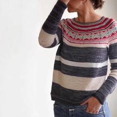 a woman wearing a sweater and jeans is holding her head in her hands while standing against a wall