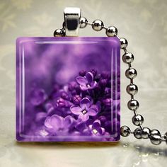 a square glass pendant with purple flowers on it's side and a silver ball chain