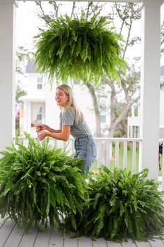 a woman standing on a porch next to two large planters filled with green plants