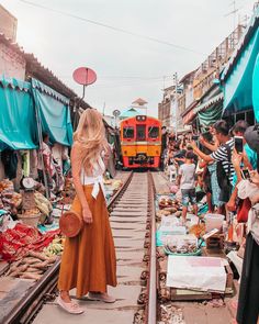 a woman is standing on the train tracks in front of an outdoor market with lots of people