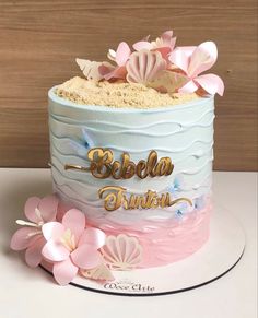 the cake is decorated with pink and blue icing, flowers, and gold lettering