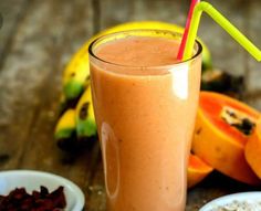 a smoothie in a tall glass with a straw next to sliced oranges and bananas