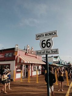 people are standing on the boardwalk next to a street sign that says santa monica 66 and end of the trail