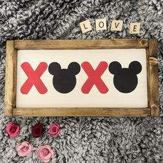 a mickey mouse sign with the words love and x on it next to some flowers