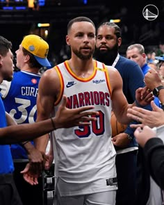 a man in a white jersey is shaking hands with some fans and other people at a basketball game