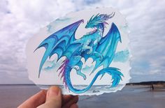 a hand holding up a piece of paper with a drawing of a blue dragon on it