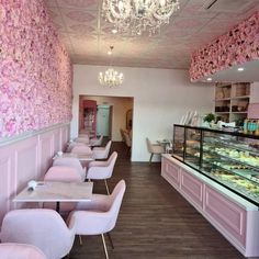 the interior of a bakery with pink flowers on the wall and white chairs in front of it