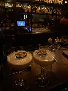 two glasses filled with drinks sitting on top of a wooden table in front of a bar