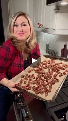 a woman holding a pan full of nuts on top of a stovetop next to an oven