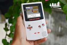 a person holding an old gameboy in their hand next to a potted plant