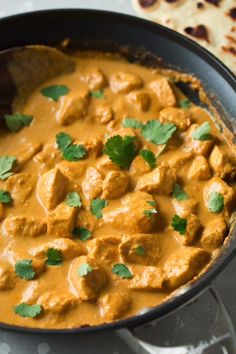 a skillet filled with chicken curry and garnished with cilantro