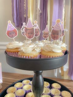 cupcakes on a cake stand in front of purple and yellow decorations with pictures of baby's faces