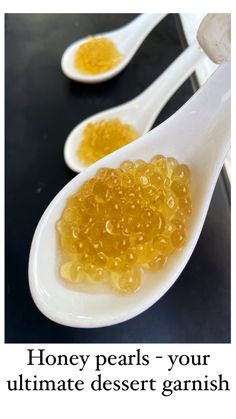 two spoons filled with honey pearls on top of a black table next to each other