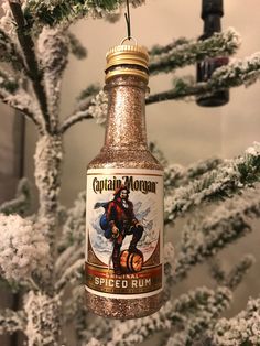 a spiced rum bottle ornament hanging from a tree with snow on it