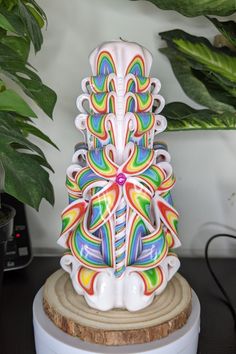 a multicolored sculpture sitting on top of a wooden stand next to a potted plant