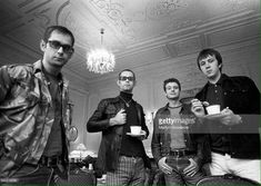 three men standing in a room holding cups and looking at the camera with one man wearing glasses