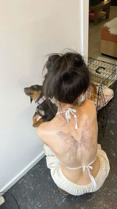 a woman sitting on the floor with her back turned to the camera, holding a small dog