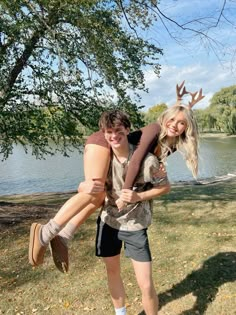 two people standing in front of a body of water, one holding the other on his back