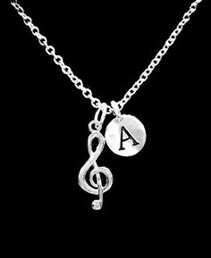 a silver necklace with a musical note and initial charm on the link, sitting on a black background