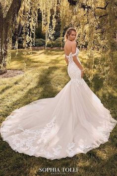 a woman in a wedding dress standing under a tree with her back turned to the camera