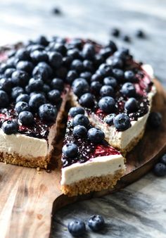 a blueberry cheesecake on a wooden board with one slice cut out and ready to be eaten