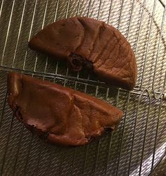 two chocolate cookies sitting on top of a cooling rack next to each other, one half eaten