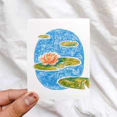 a person holding up a card with a drawing of a water lily on it's side