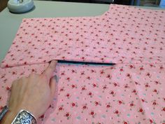 a person cutting fabric with a knife on top of a pink table cloth that has flowers all over it