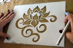 two hands are drawing on a piece of white paper with gold foil and a black marker